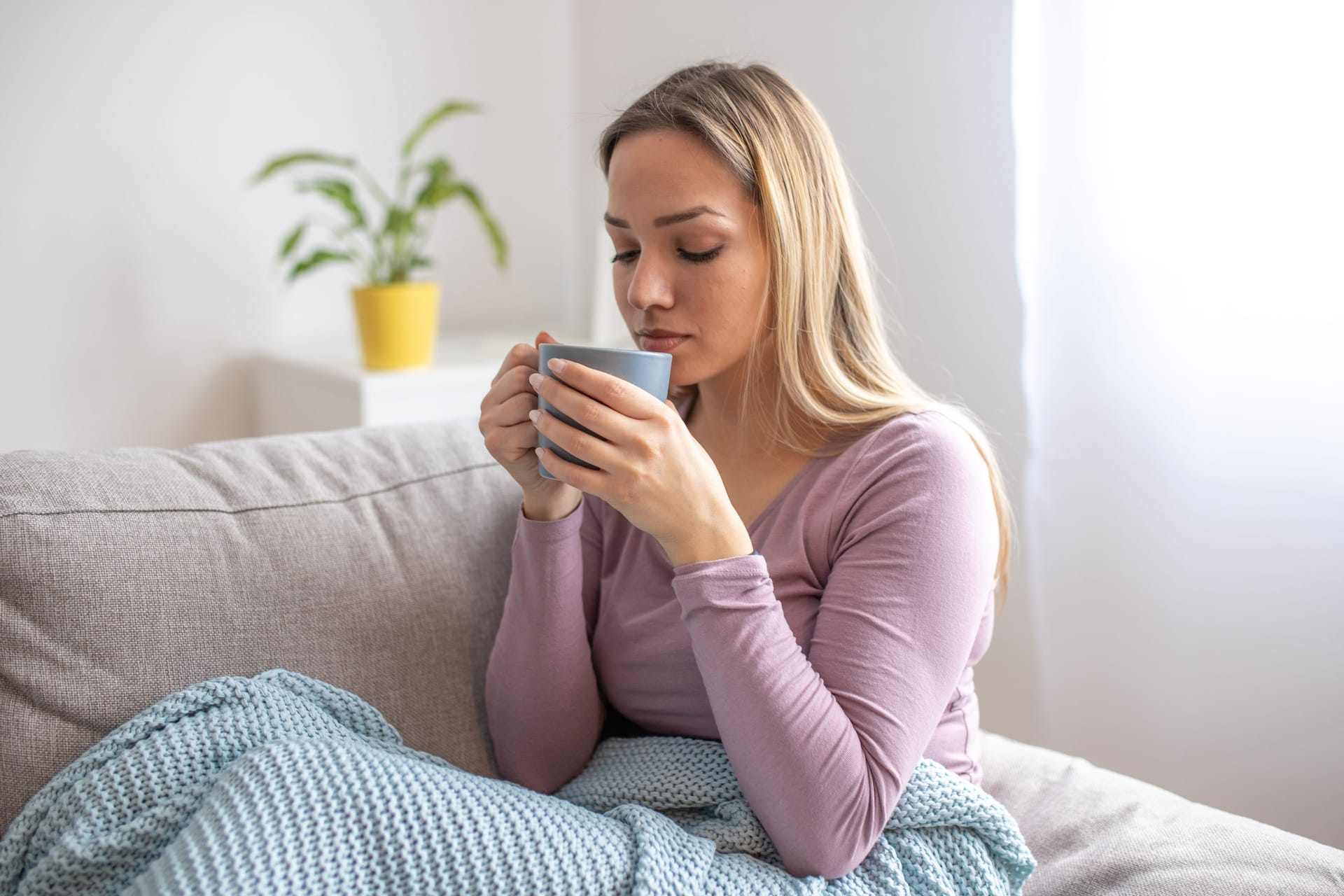 Junge Frau sitzt auf dem Sofa und trinkt Tee.