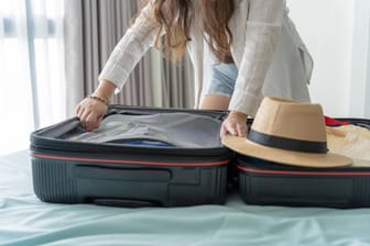 Eine Frau packt ihren Koffer auf einem Hotelbett aus (Symbolbild): In anderen Städten gibt es die Übernachtungssteuer bereits.