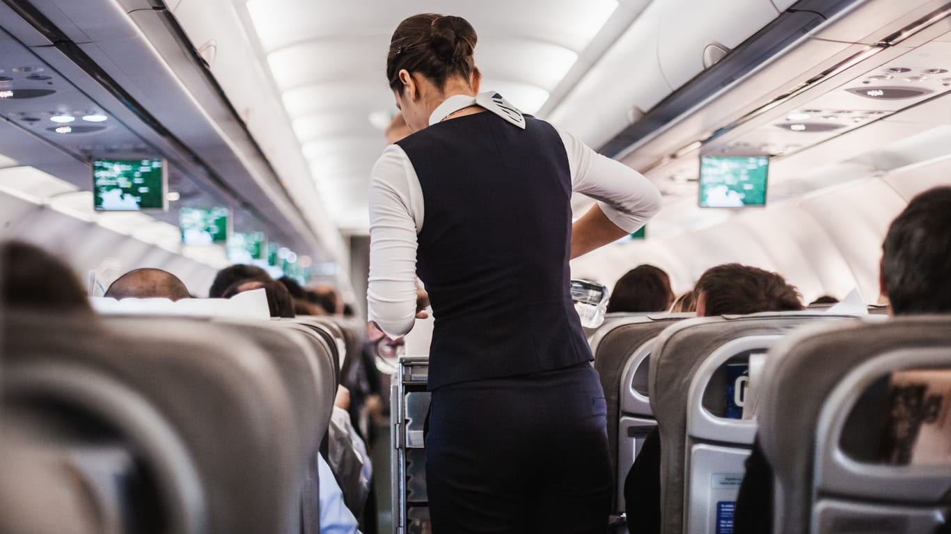 Eine Stewardess geht mit einem Getränkewagen durch ein Flugzeug (Symbolbild): Den Mann erwarten nun mehrere Anzeigen.