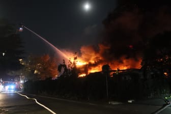 Feuerwehrleute kämpfen gegen den Brand in einer Lagerhalle an der Meteorstraße an.