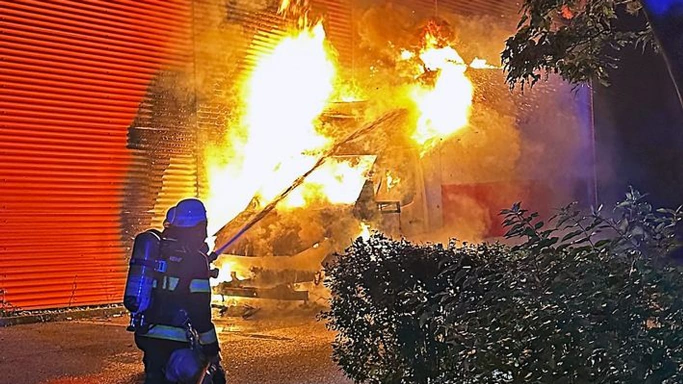 Hohe Flammen schlagen aus dem Auto: Ein Feuerwehrmann löscht einen Kleintransporter in der Nacht.