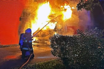 Hohe Flammen schlagen aus dem Auto: Ein Feuerwehrmann löscht einen Kleintransporter in der Nacht.