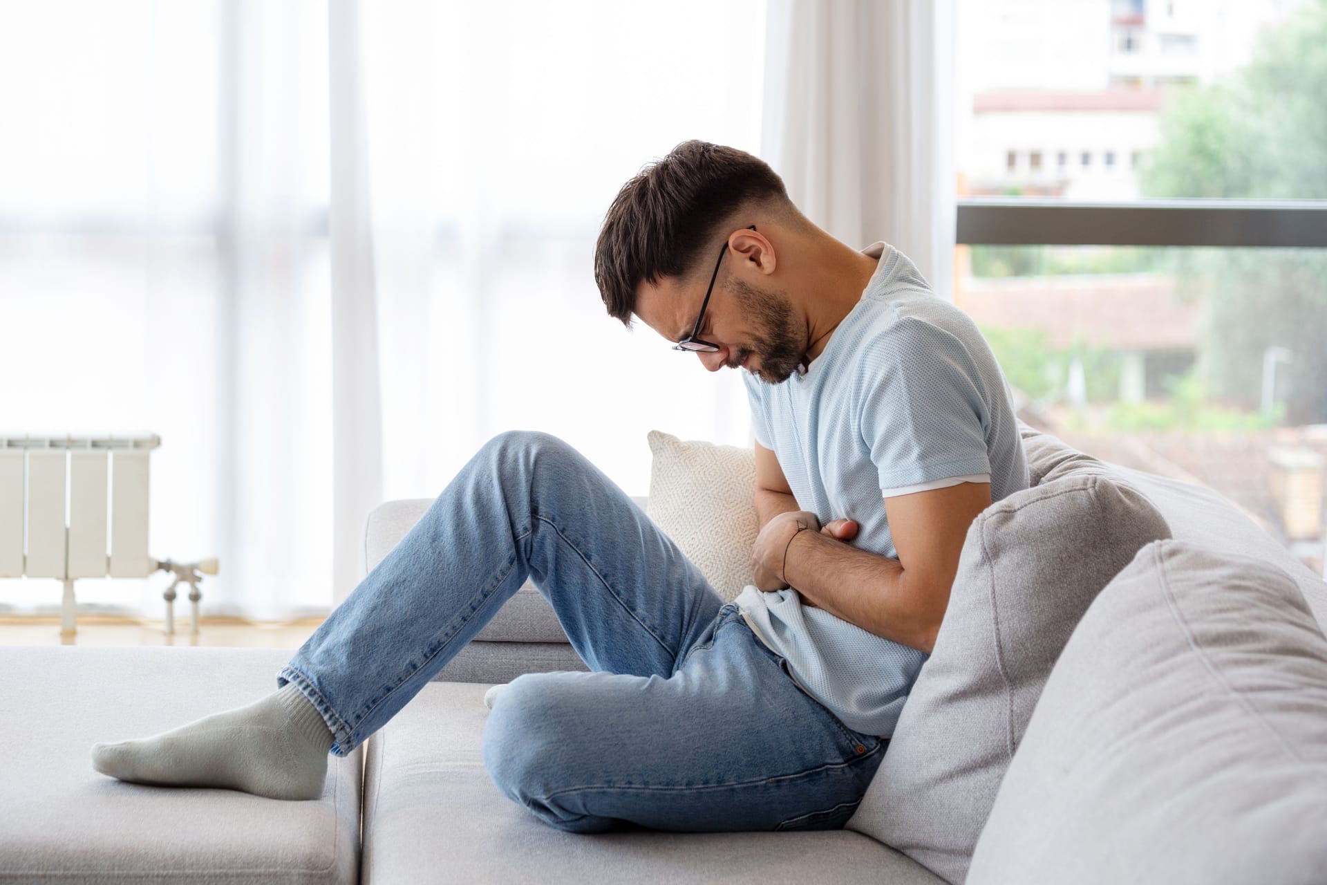 Ein Mann sitzt mit Bauchweh auf dem Sofa