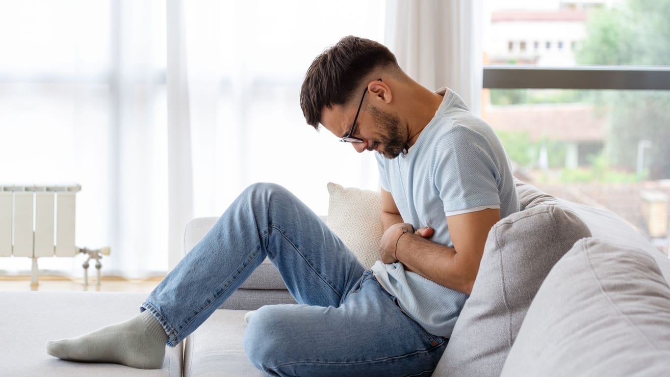 Ein Mann sitzt mit Bauchweh auf dem Sofa