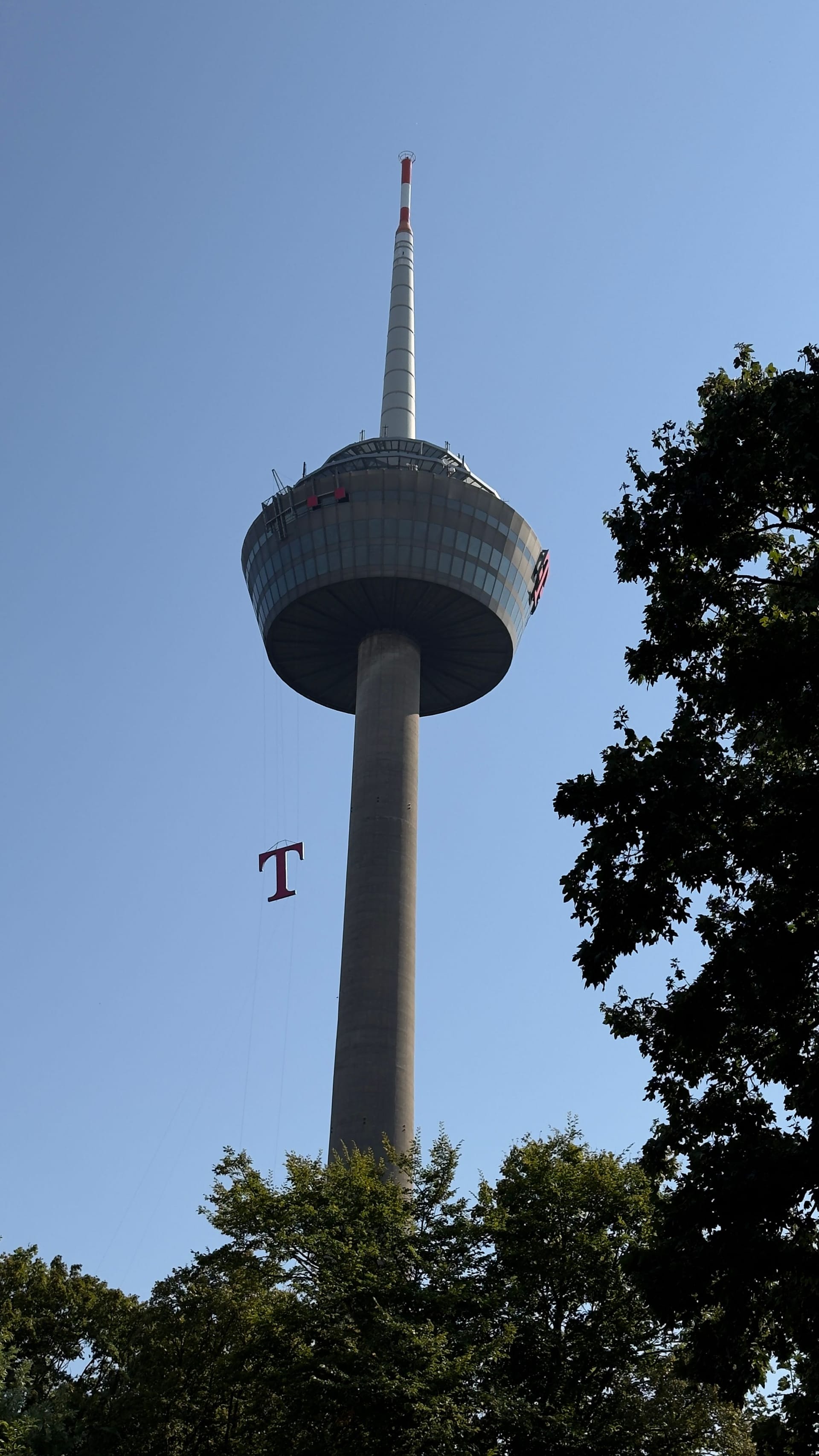 Das neue Logo am Kölner Fernsehturm Colonius wird hochgezogen. Die Telekom hat den Bereich um den Kölner Fernsehturm großräumig abgesperrt.