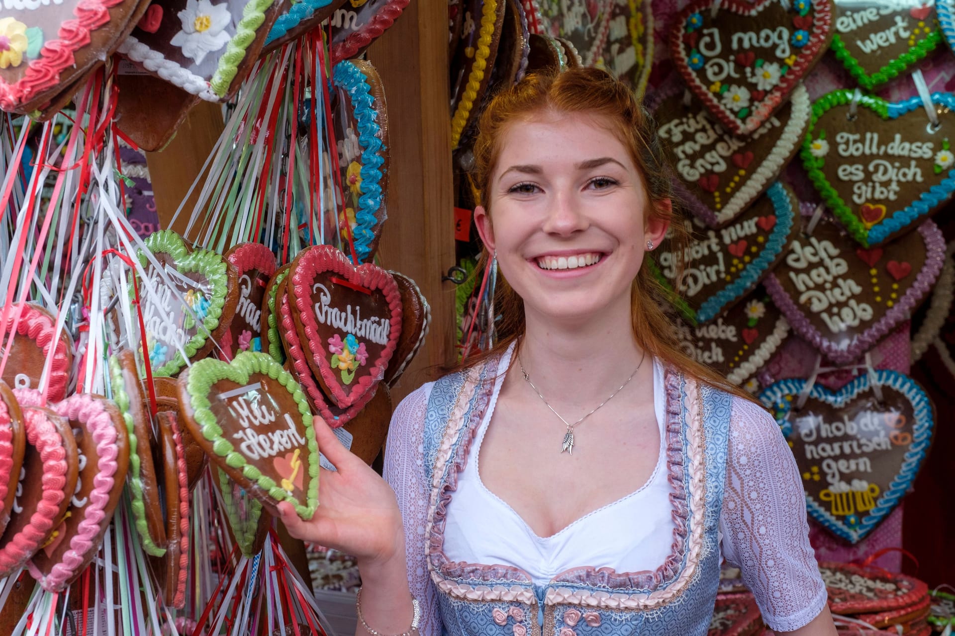 Bairisch auf dem Oktoberfest: Ein Frau steht an einem Lebkuchenstand. Die Aufschriften auf den Herzen sind in Dialekt verfasst - zum Beispiel: "I mog di" ("Ich mag dich").