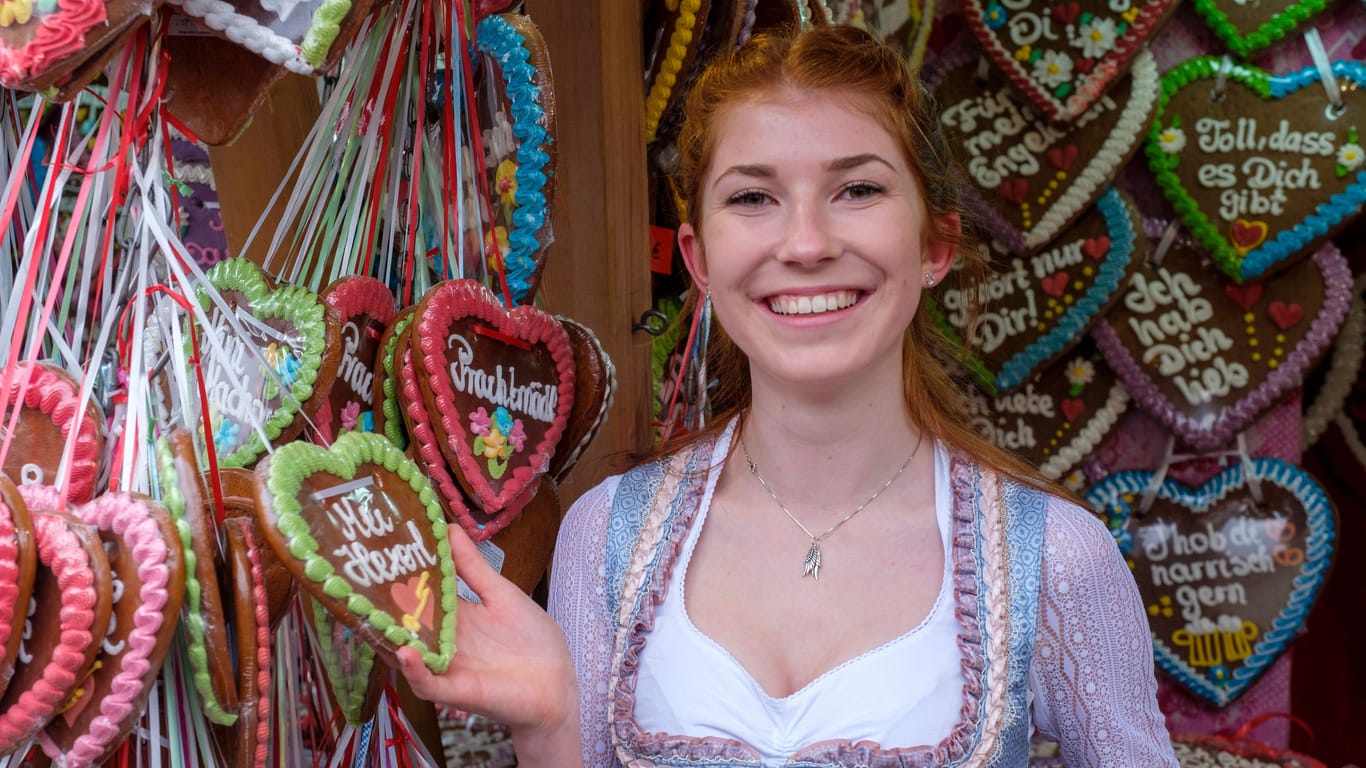 Bairisch auf dem Oktoberfest: Ein Frau steht an einem Lebkuchenstand. Die Aufschriften auf den Herzen sind in Dialekt verfasst - zum Beispiel: "I mog di" ("Ich mag dich").