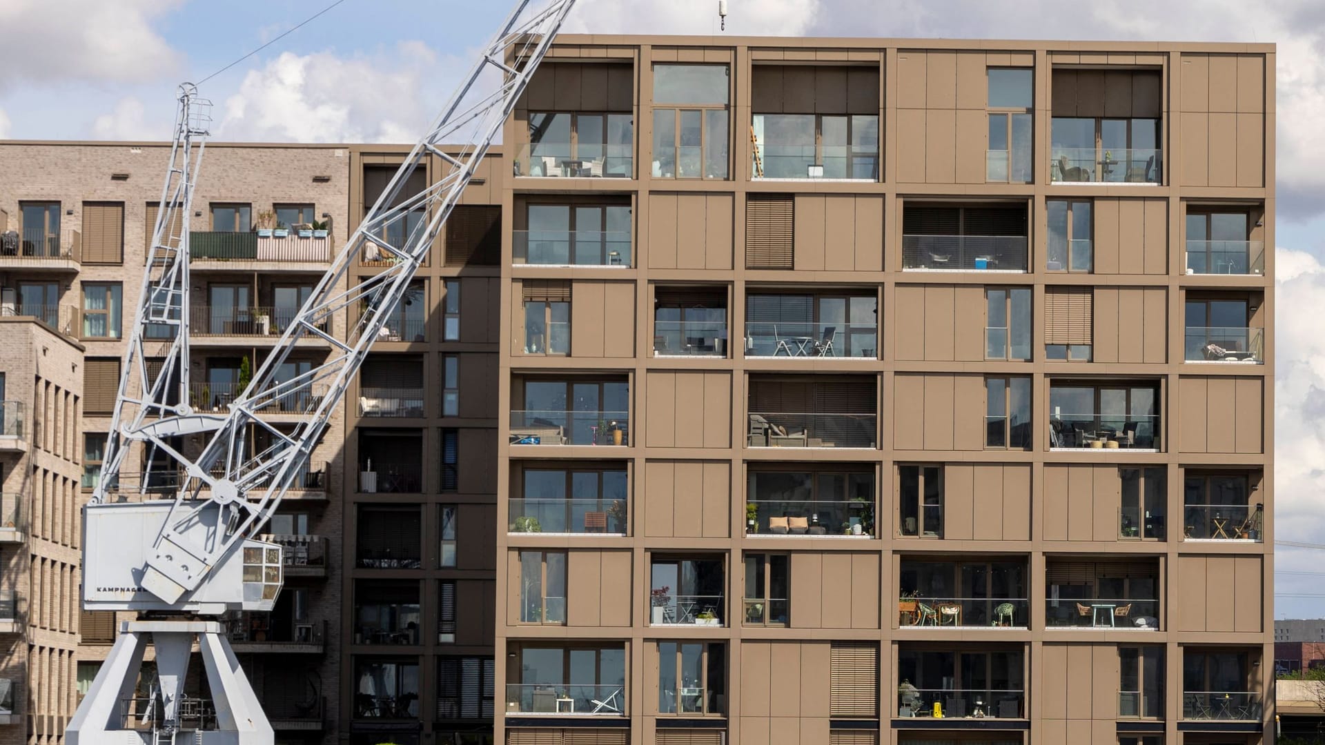Das Bild zeigt neu gebaute Häuser am Baakenhafen in der Hafencity in Hamburg. Links stehen zwei braune Häuser, rechts ein weißes. Zu sehen ist jeweils eine große Fensterfront. Vor den Häusern stehen zwei weiße Kräne. Der Himmel ist bewölkt und blau. Das Bild zeigt neu gebaute Häuser am Baakenhafen in der Hafencity in Hamburg. Links stehen zwei braune Häuser, rechts ein weißes. Zu sehen ist jeweils eine große Fensterfront. Vor den Häusern stehen zwei weiße Kräne. Der Himmel ist bewölkt und blau.