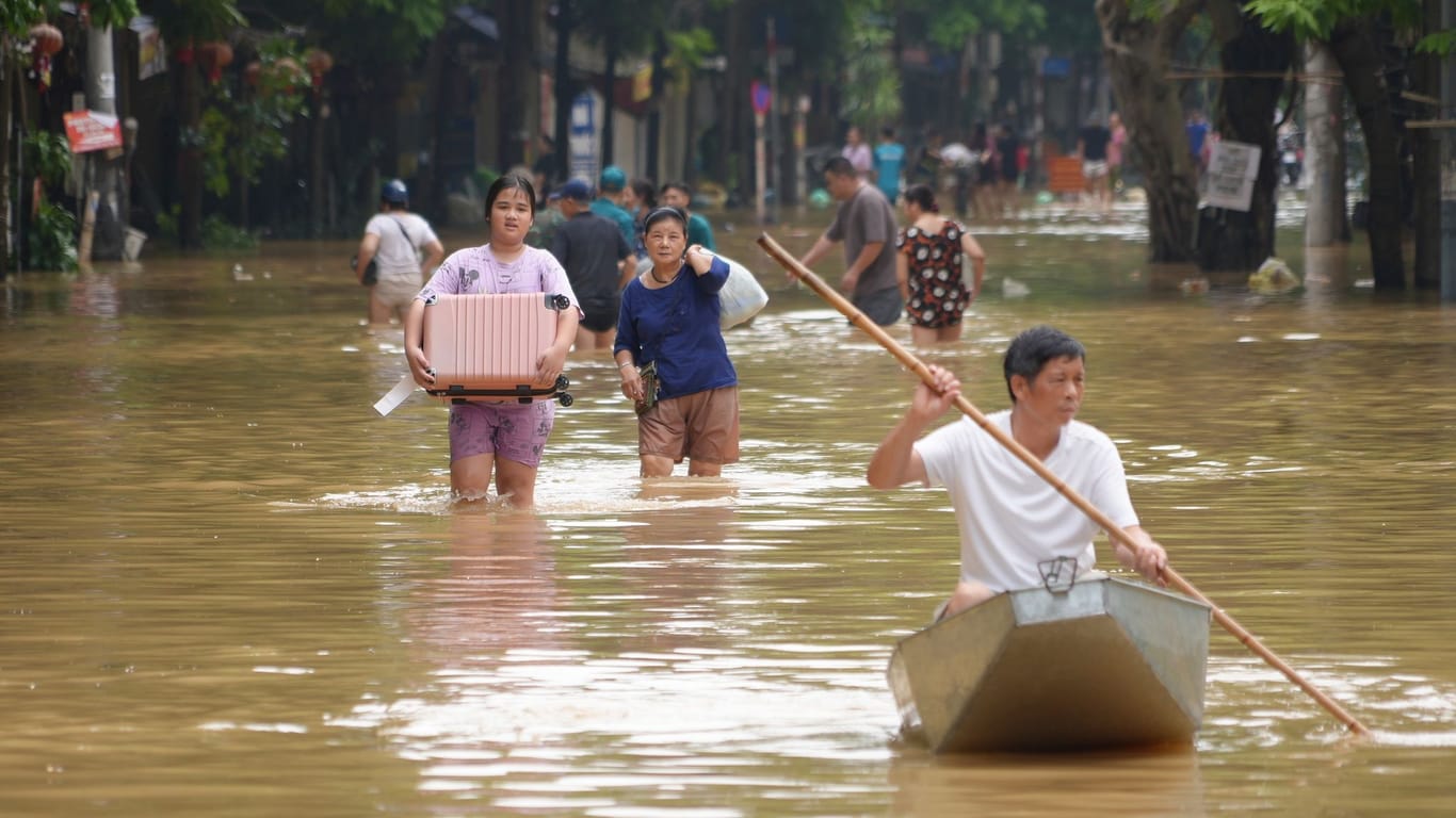 Hanoi: Menschen, die Habseligkeiten tragen, waten durch eine überflutete Straße der vietnamesischen Hauptstadt.