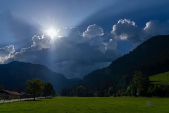 Bad Hindelang im Oberallgäu: Die Sonne sendet ihre letzten Strahlen aus, bevor sie von einer Gewitterwolke verschluckt wird.