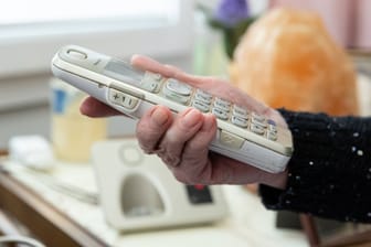 Eine Seniorin hält ein Telefon (Archivbild): In Dresden wurden zwei über 80-Jährige betrogen.