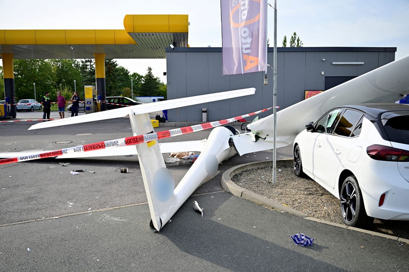 Ein abgestürztes Segelflugzeug liegt auf dem Gelände einer Tankstelle.