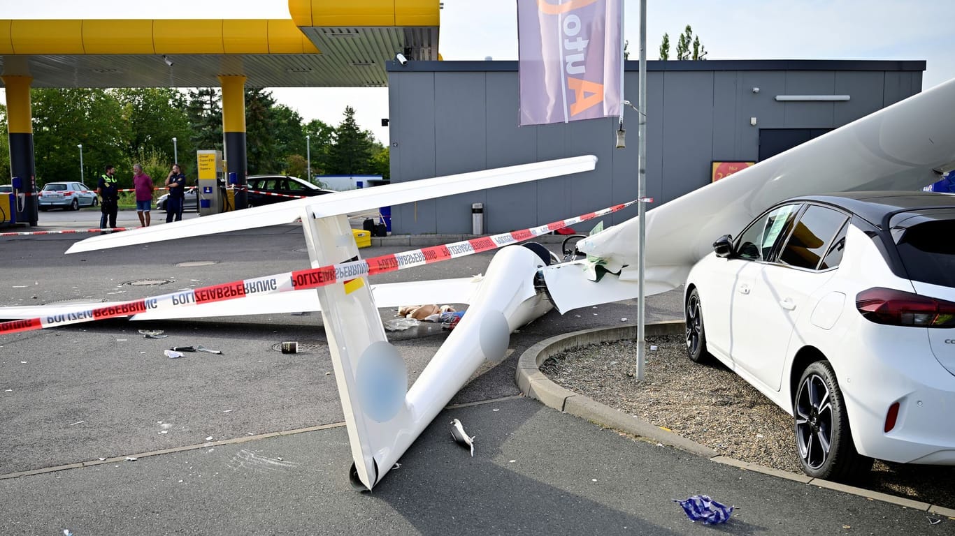 Ein abgestürztes Segelflugzeug liegt auf dem Gelände einer Tankstelle.