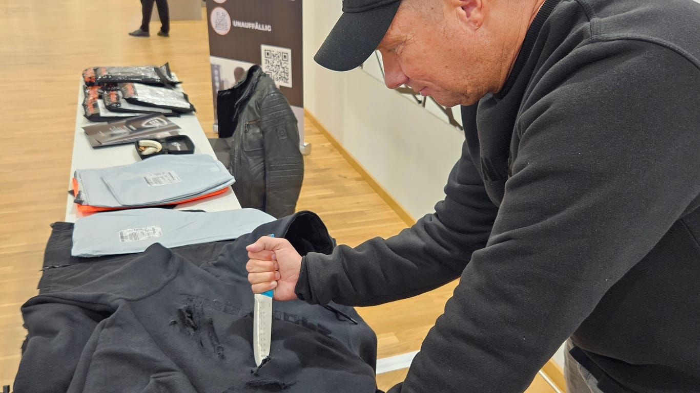 Monty Hering sticht mit einem Messer in einen seiner Hoodies. Die oberste Stoffschicht kann dabei beschädigt werden, in die Haut dringt die Klinge jedoch nicht ein.