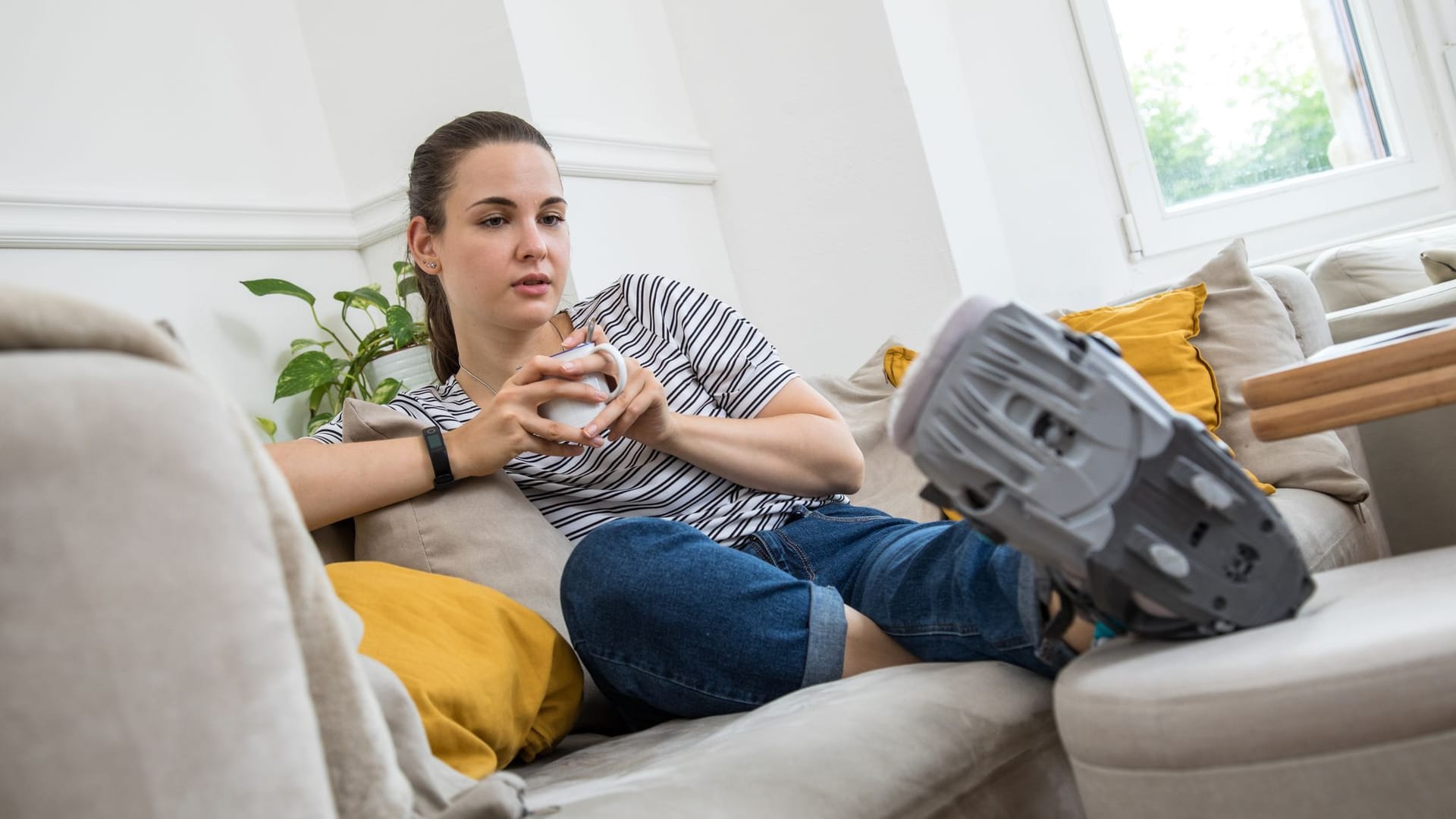 Eine Frau liegt mit einer Orthese auf dem Sofa