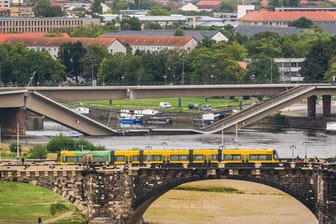 Blick auf die eingestürzte Carolabrücke während im Vordergrund eine Straßenbahn über die Augustusbrücke fährt: