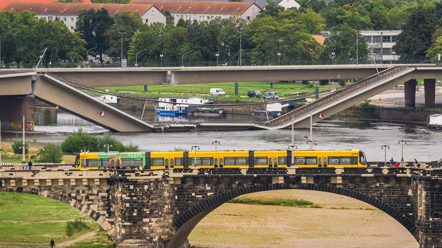 Blick auf die eingestürzte Carolabrücke während im Vordergrund eine Straßenbahn über die Augustusbrücke fährt: