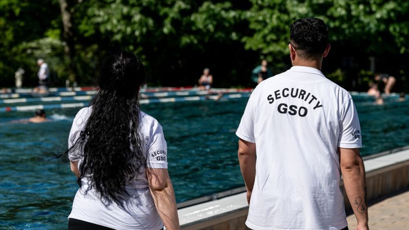 Security-Mitarbeiter laufen im Sommerbad Kreuzberg am Rand des Sportbeckens: