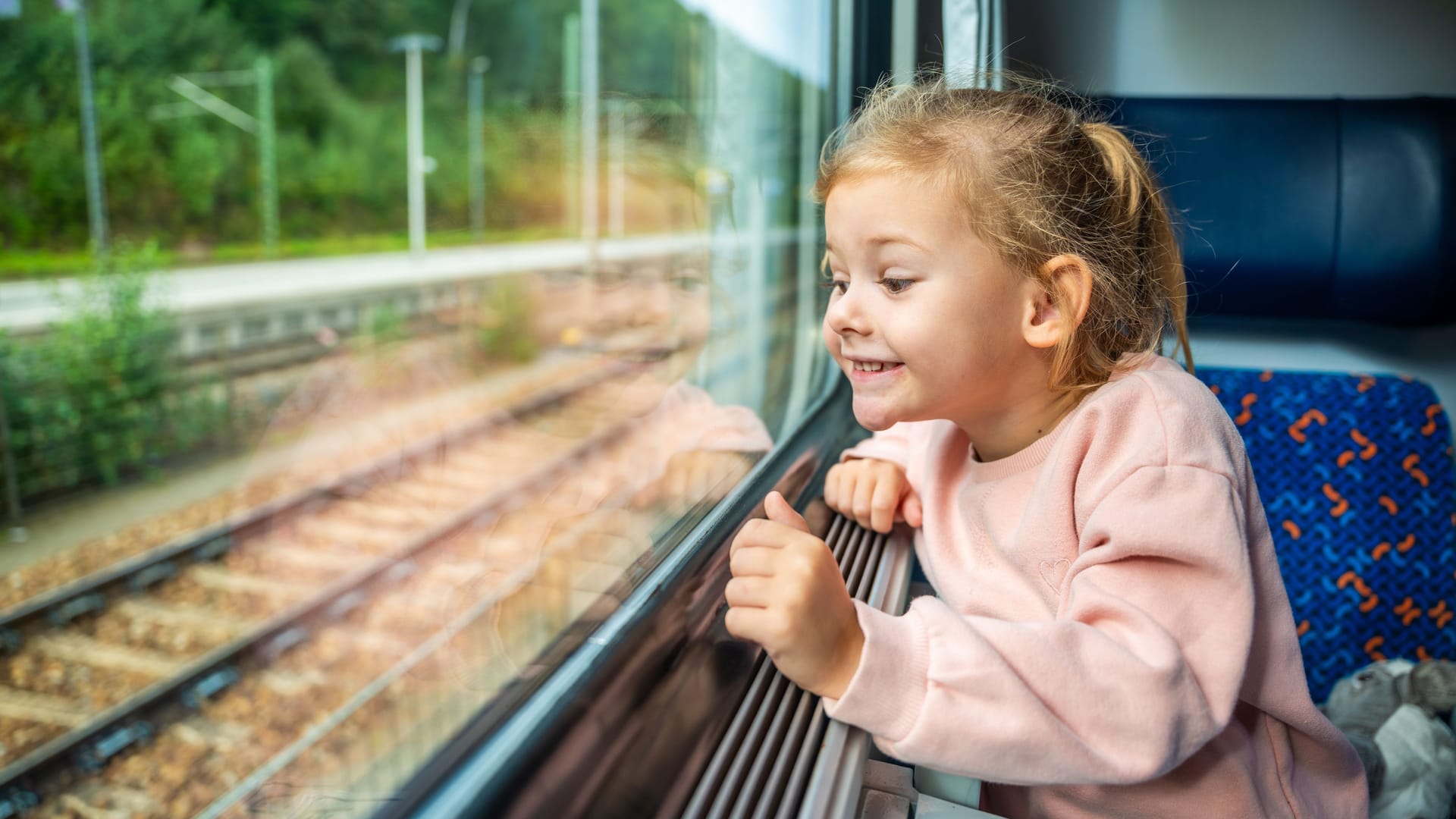 Happy little girl looking out train window outside, while it moving. Traveling by railway, Europe