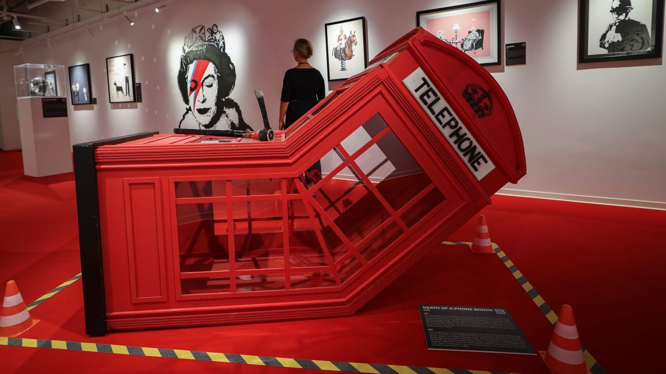 Eine Frau geht durch einen Raum mit der Skulptur "Death Of Telephone Booth": Die Banksy-Ausstellung Motive des Street-Art-Künstlers als Reproduktionen.