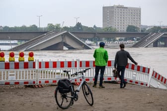 Zwei Männer stehen vor der vom Hochwasser der Elbe umspülten teileingestürzten Carolabrücke: Die Brücke ist weiträumig abgesperrt.