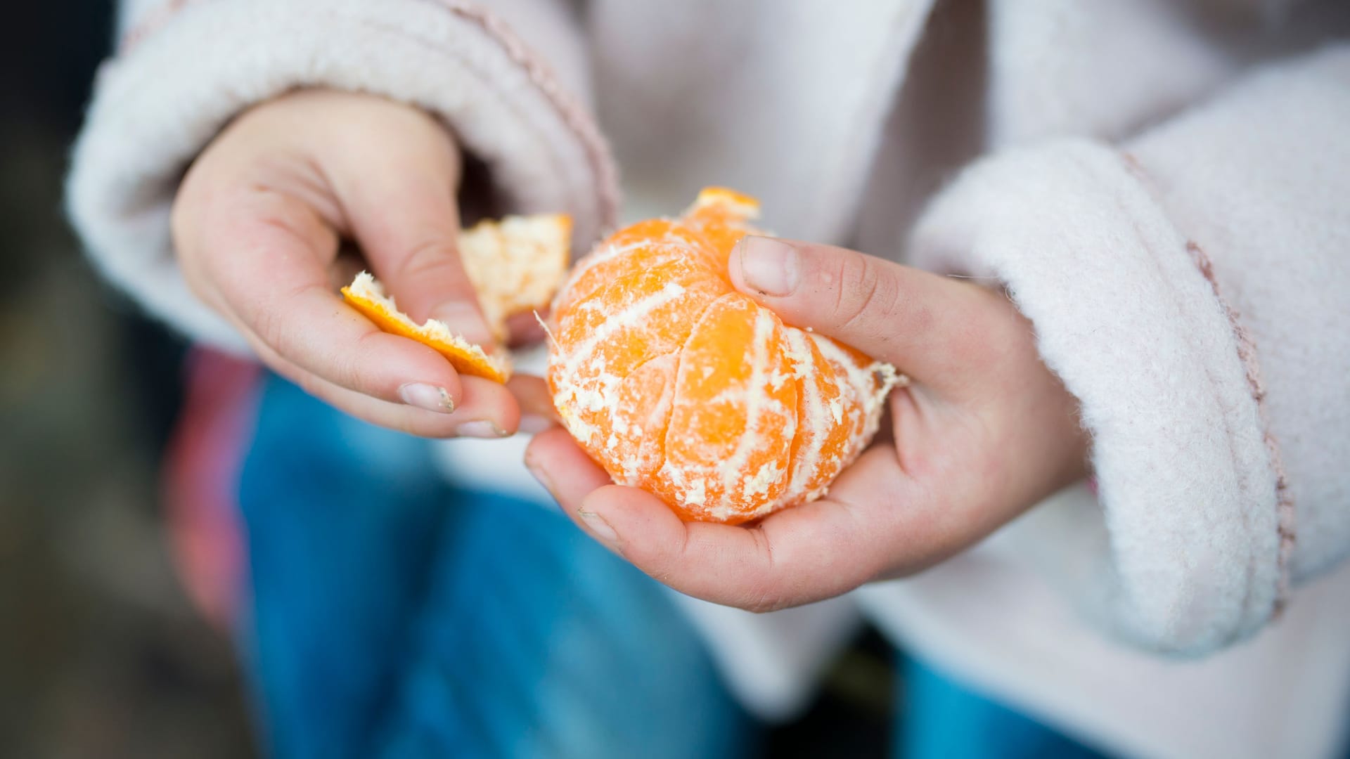 Ein Kind schält eine Mandarine.