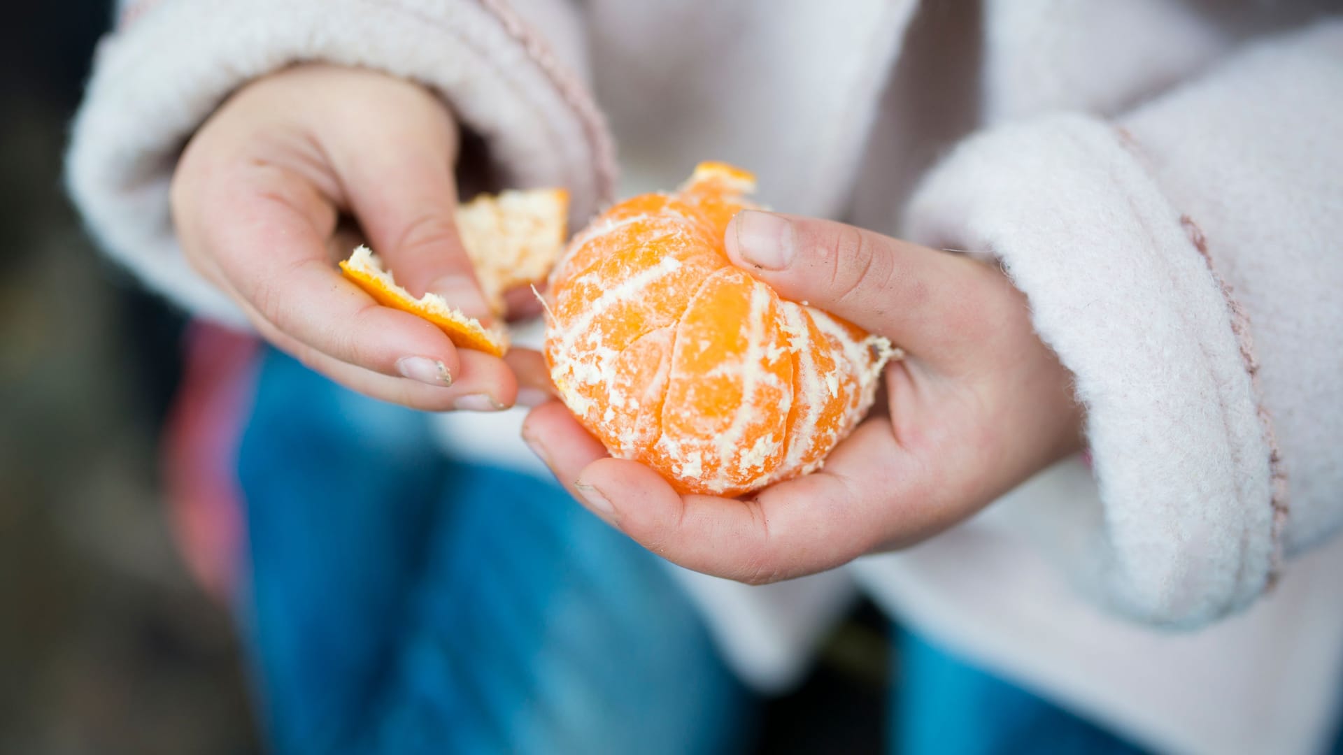 Ein Kind schält eine Mandarine.