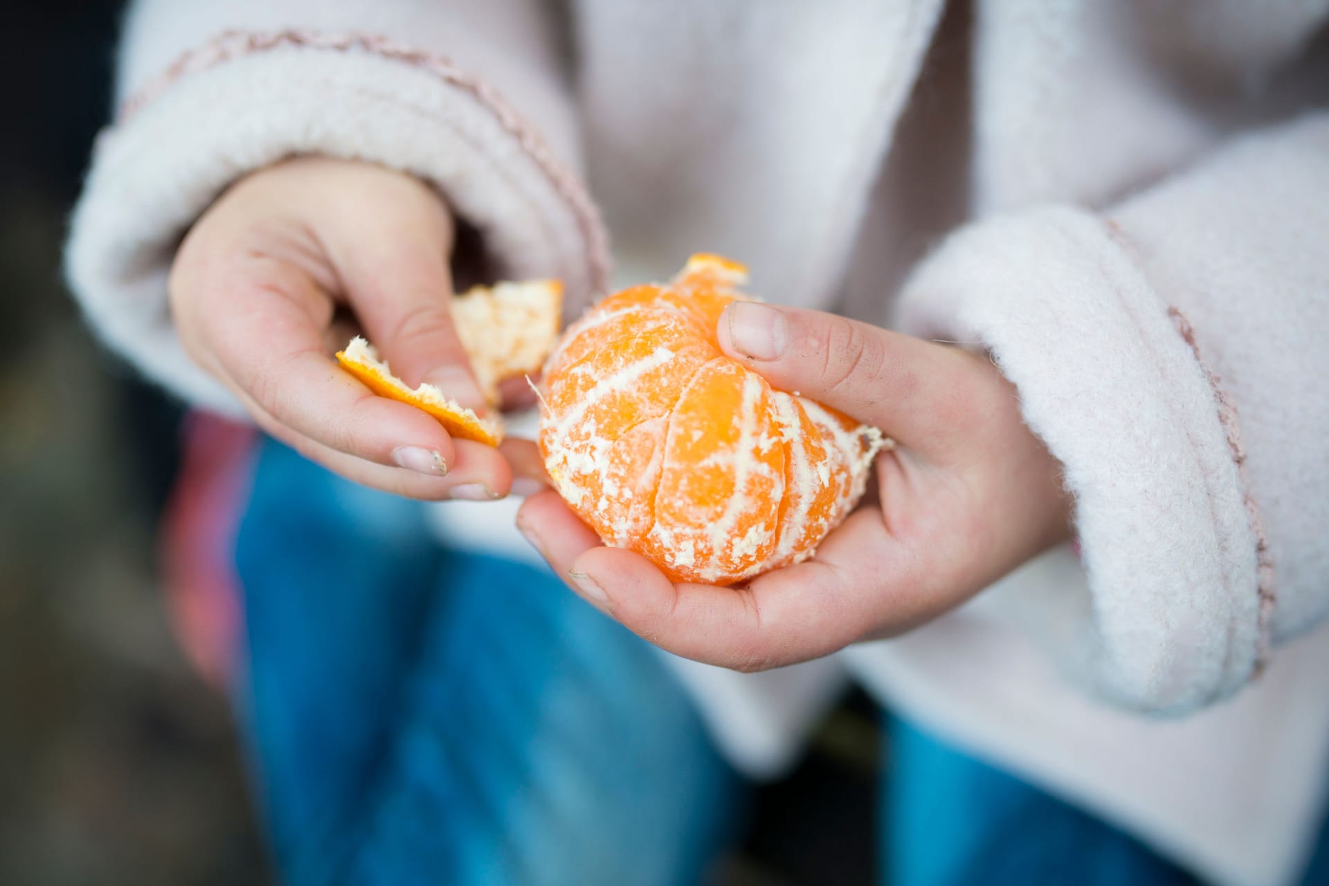 Ein Kind schält eine Mandarine.