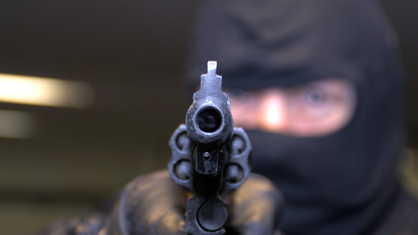 Ein maskierter Mann hält eine Waffe (Symbolbild): Zu einem bewaffneten Überfall ist es am Dienstag in einer Tankstelle gekommen.