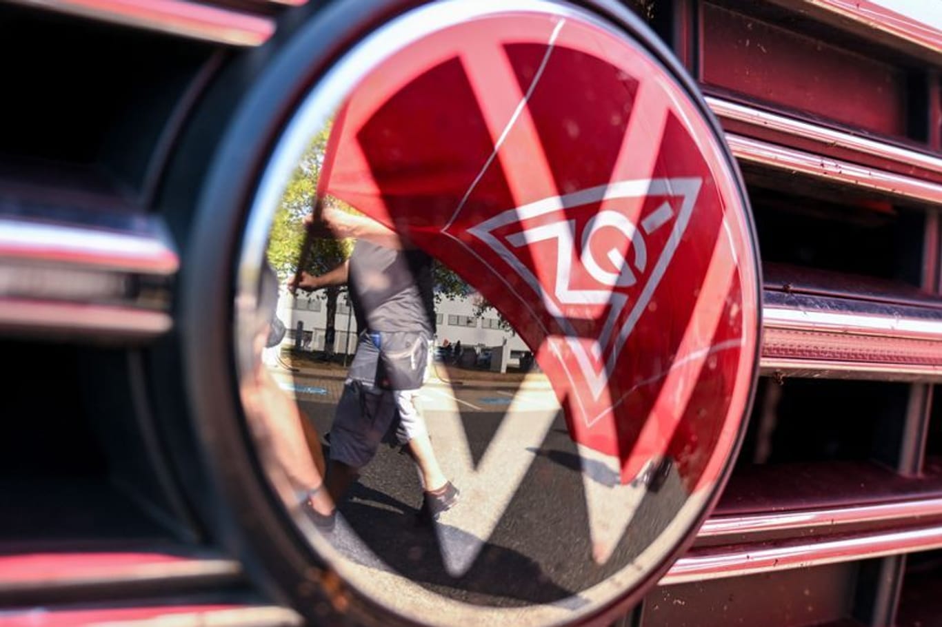 VW Logo, in dem sich die Fahne der IG Metall spiegelt