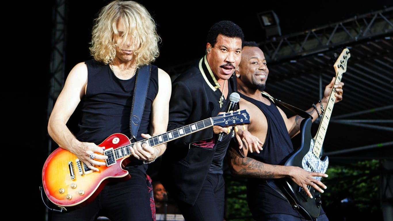 Lionel Richie (m.) steht zwischen zwei seiner Musiker beim Stadtpark Open Air auf der Freilichtbühne im Stadtpark Hamburg. (Archivbild von 2016)