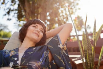 Frau sitzt im Garten und genießt die Sonne