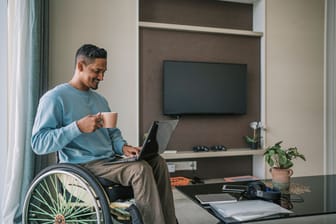 Mann sitzt im Rollstuhl und arbeitet auf seinem Laptop