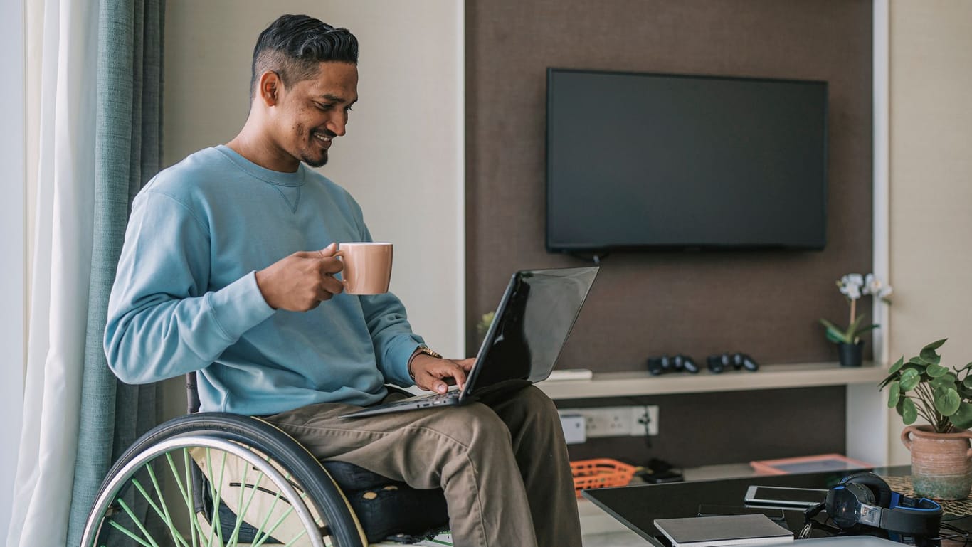 Mann sitzt im Rollstuhl und arbeitet auf seinem Laptop