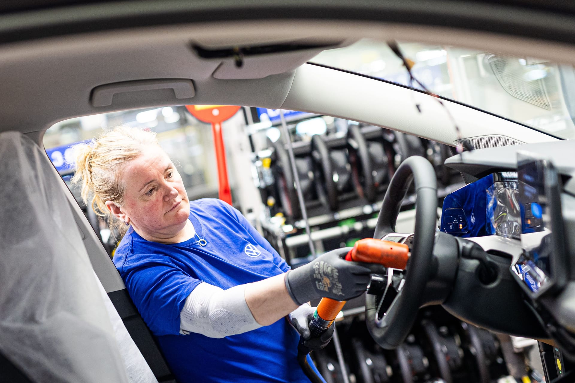 Eine Mitarbeiterin montiert in einem Fahrzeug im VW-Werk ein Lenkrad.