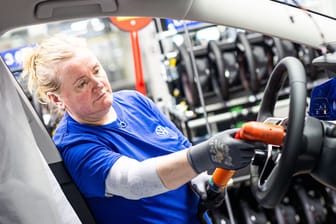 Eine Mitarbeiterin montiert in einem Fahrzeug im VW-Werk ein Lenkrad.