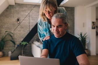 Ein Paar blickt auf einen Laptop: Kombinieren Verheiratete ihre Steuerklassen richtig, können sie ihr Monatseinkommen aufbessern.