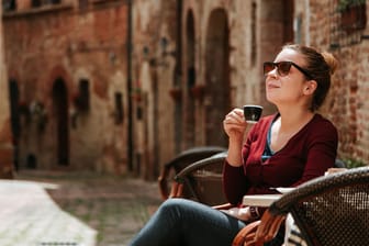 Eine Frau genießt einen Espresso in Italien: Wer dauerhaft ins Ausland zieht, sollte wissen, worauf er sich steuerlich einlässt.