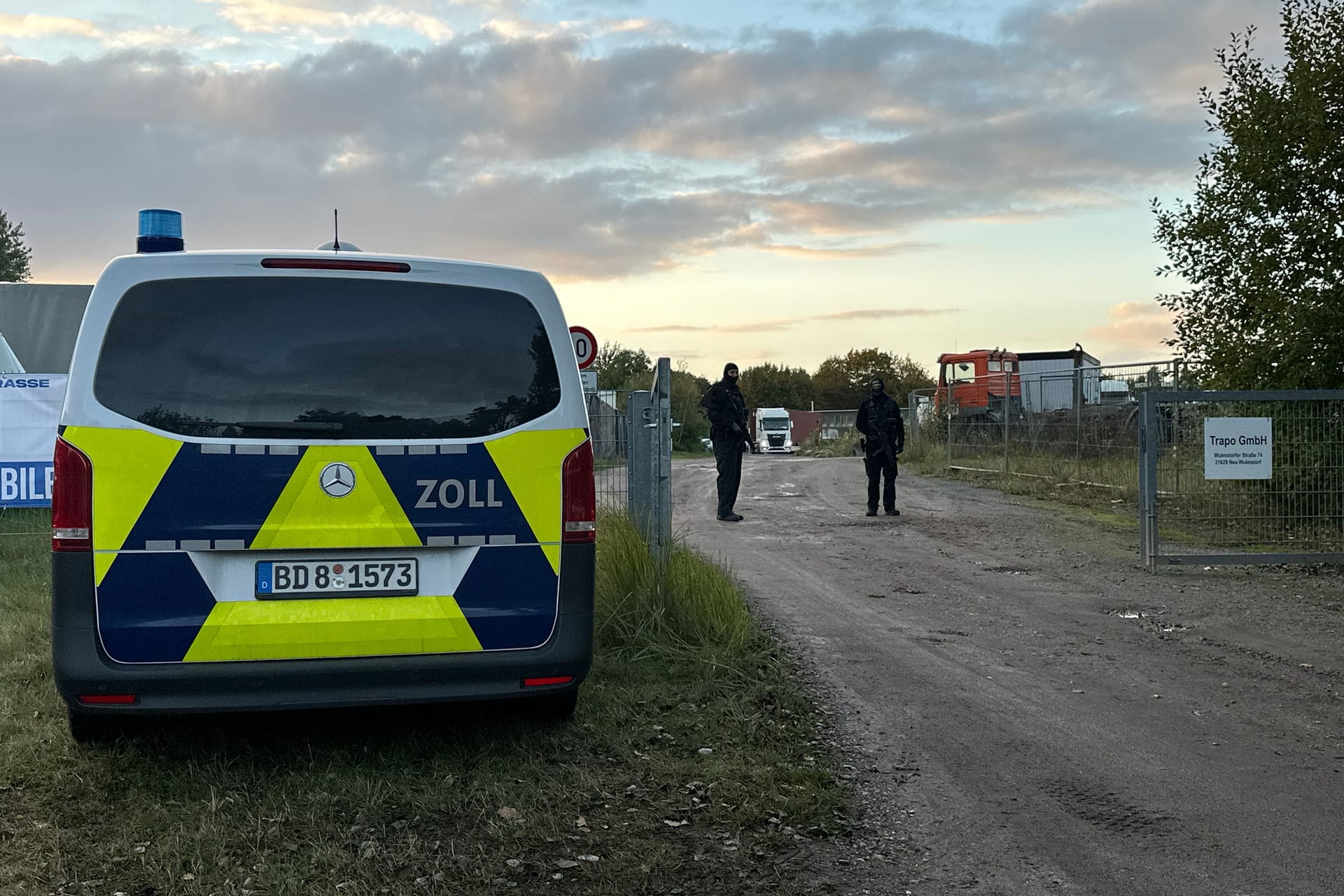 Ein Einsatzwagen der Polizei und schwarz gekleidete Beamte stehen vor dem Gelände an der Wulmsdorfer Straße.