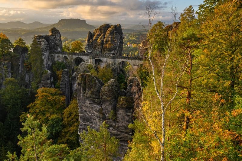 Sonnenlicht fällt am Morgen auf die herbstlich gefärbten Bäume im Nationalpark Sächsische Schweiz nahe der Basteibrücke: Das sächsische Klettern folgt eigenen Regeln.