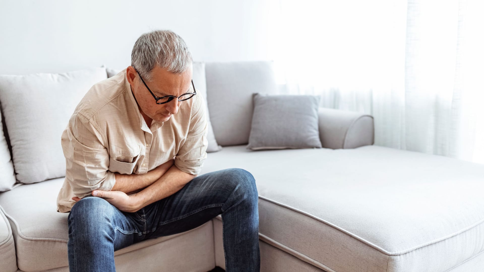 Ein Mann sitzt mit Bauchweh auf dem Sofa.