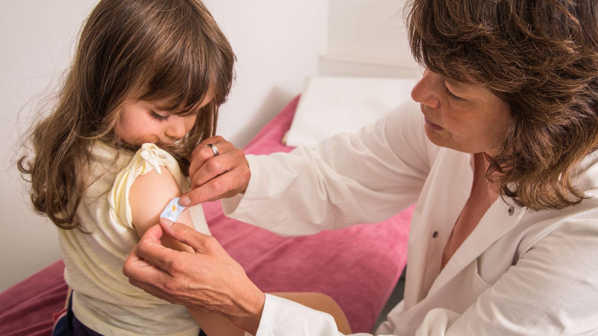 Mädchen bekommt beim Kinderarzt ein Pflaster auf den Arm