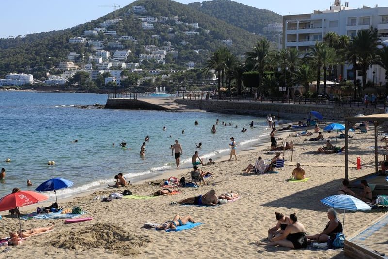 Menschen sonnen sich am Strand von Santa Eulalia auf Ibiza.