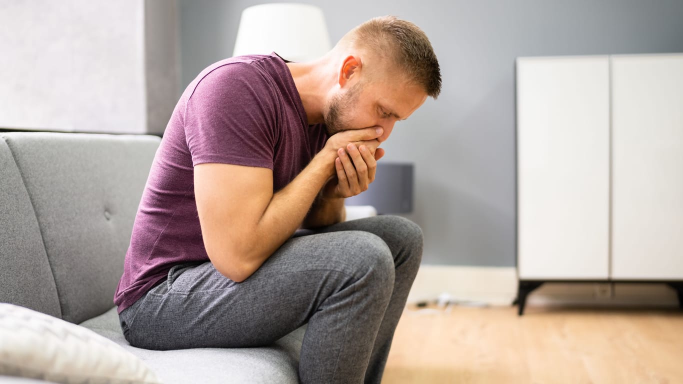 Junger Mann sitzt auf dem Sofa und leidet unter Übelkeit