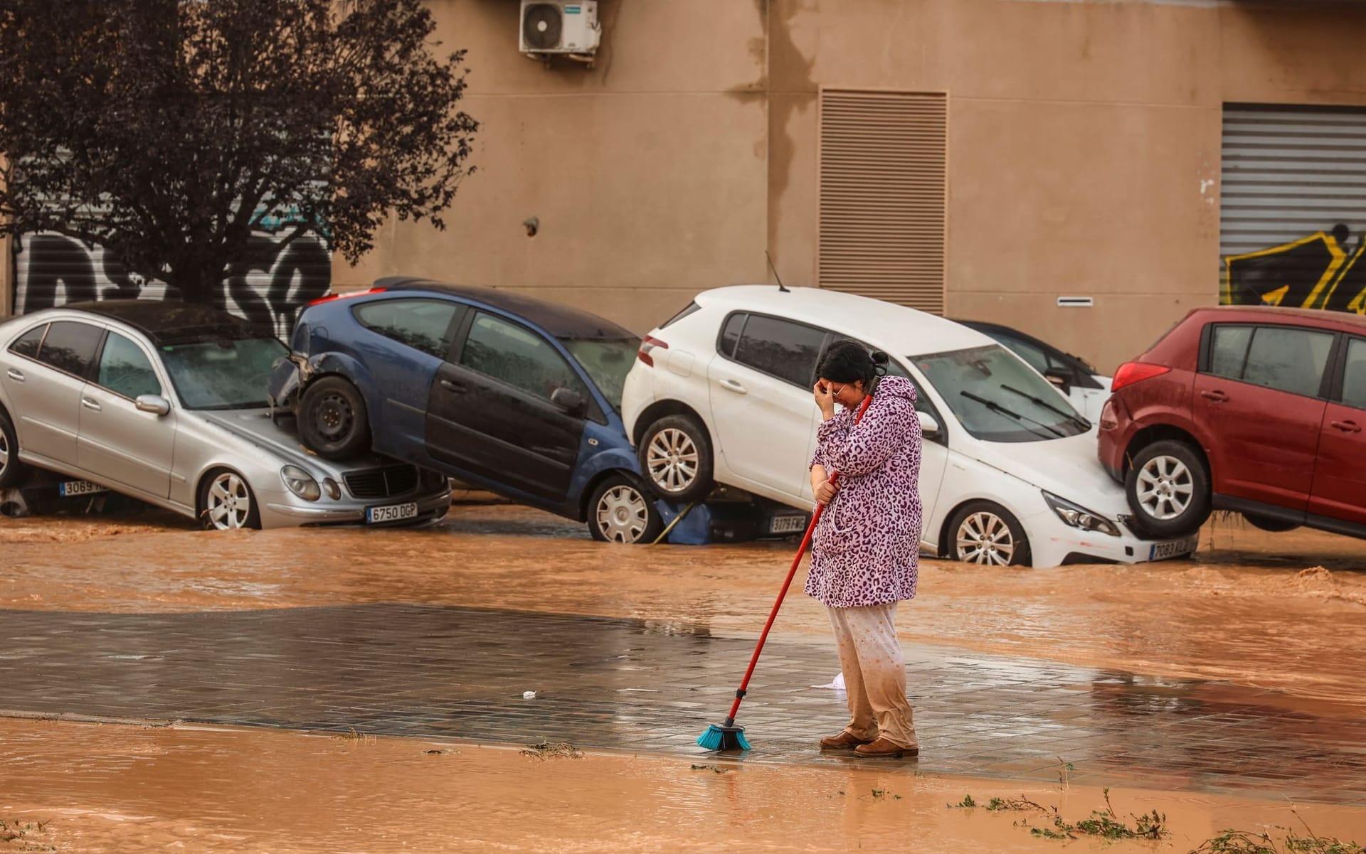 Eine Frau steht mit einem Besen auf einer Straße neben Autowracks in Valencia.