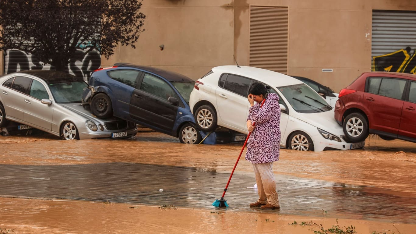 Eine Frau steht mit einem Besen auf einer Straße neben Autowracks in Valencia.