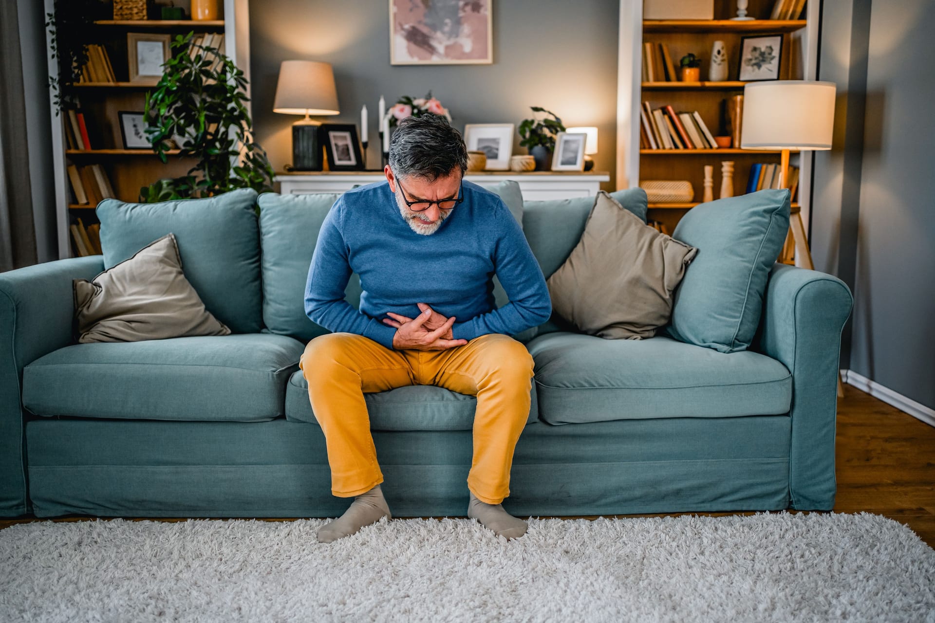 Ein Mann sitzt mit Bauchweh auf dem Sofa