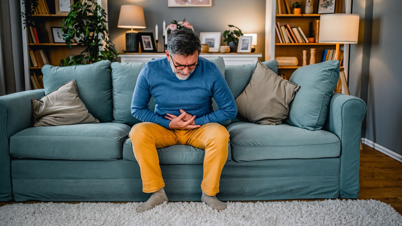 Ein Mann sitzt mit Bauchweh auf dem Sofa