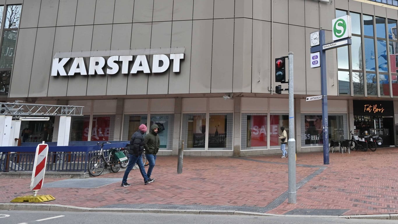 Das frühere Karstadt-Haus in Hamburg-Harburg (Archivbild). Das Bild zeigt das Gebäude von außen. Im Vordergrund ist eine S-Bahnstation sichtbar. Menschen gehen vor dem Kaufhaus vorbei. Der Himmel ist blau und bewölkt.