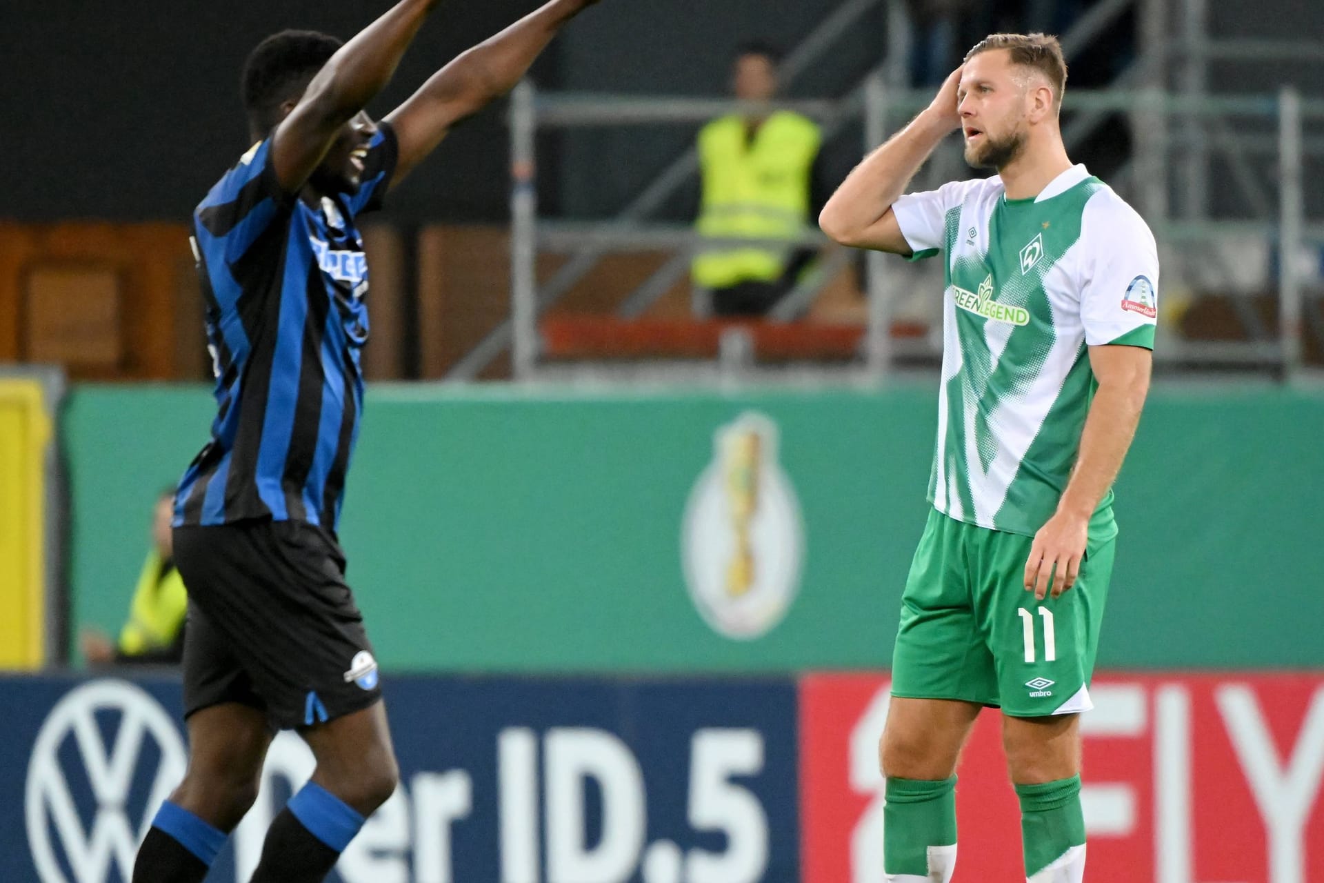 Paderborns Spieler Sirlord Conteh (l.) jubelt, er streckt die Arme gerade nach oben in die Luft. Rechts von ihm steht Werder Bremens Nicklas Füllkrug, der sich enttäuscht die rechte Hand an das Gesicht hält.